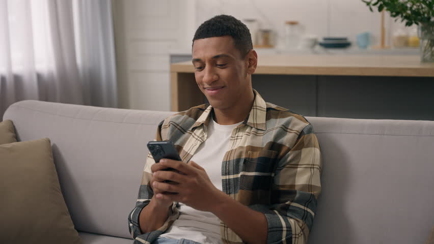Happy smiling African American man relax on sofa at home smile laugh looking mobile phone screen smartphone chat browsing telephone ethnic guy biracial male watching funny video online fun laughing Royalty-Free Stock Footage #3441902525