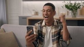 Wow African American man surprised wonder amazed win with phone mobile shocked sudden victory good winning news biracial male ethnic guy celebrating online success achieve offer excited on sofa couch - Powered by Shutterstock - Get 15% off with code: PIKWIZARD15