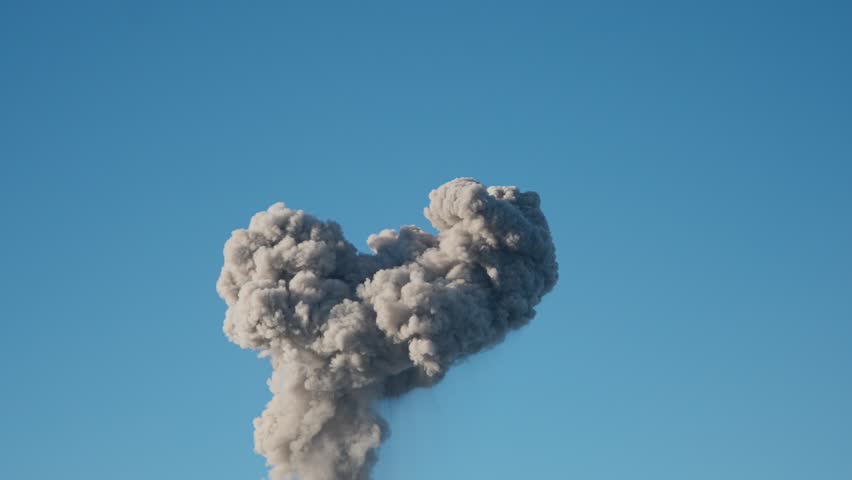 Explosion causes mushroom cloud to rises into blue sky in war zone