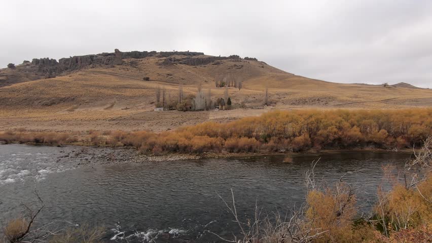 Idyllic landscape. Rurality. Panorama view of the river flowing across the yellow grassland and mountains. View of a rustic ranch in the valley.