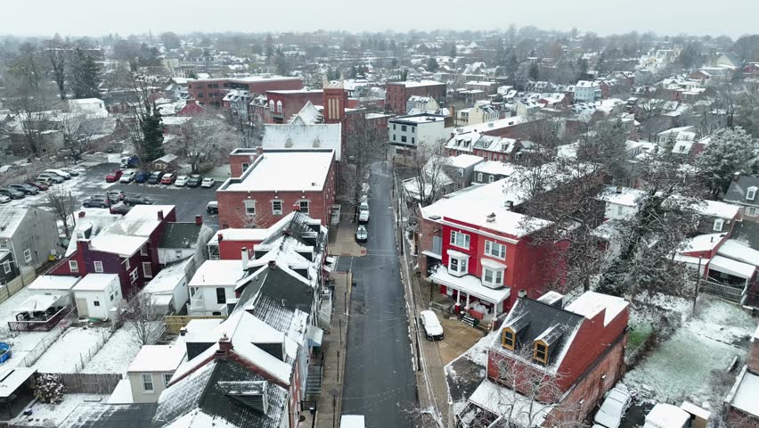American city during snow flurries. Aerial view of a snowy street with lined cars and red brick houses.
