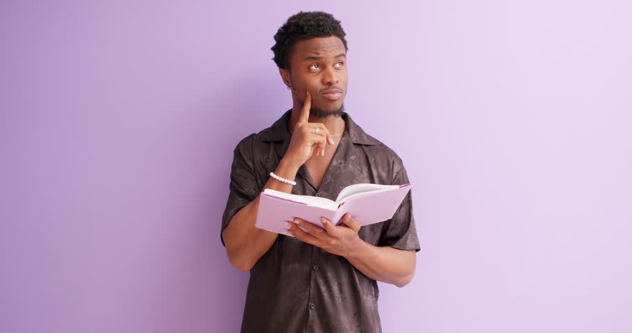 young man holding book, studing, trying to remember new information, pensive guy with finger on his cheek thinking about information of text, man making up plan, idea closeup portrait