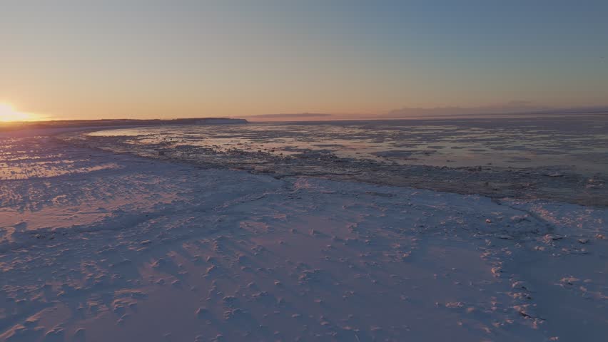 Colorful sunset over a frozen lake and snowy shore in Alaska. Aerial drone view