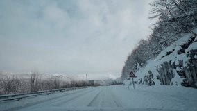 POV video of driving through Norway's Western Fjords in winter, showcasing a journey along snowy roads. The route offers scenic views of towering mountains and majestic fjords amidst heavy snowfall