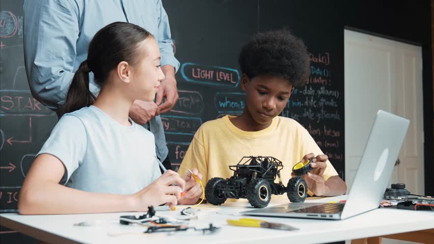 Caucasian teacher pointing at laptop screen while explain car model system at blackboard with coding or programming code written. Happy diverse student learning about robotic construction. Edification Royalty-Free Stock Footage #3442075191