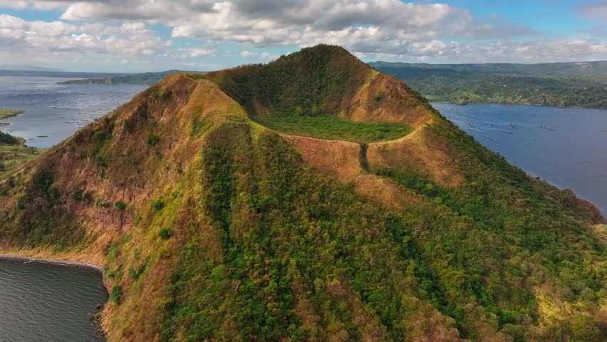 Taal Volcano Crater lighting in sunlight with Taal Lake and Fishing cages in background. Aerial rising tilt down.