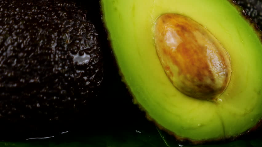 Drops of water fall on avocado fruits with leaves on a black background. Raw Fruits, healthy food.