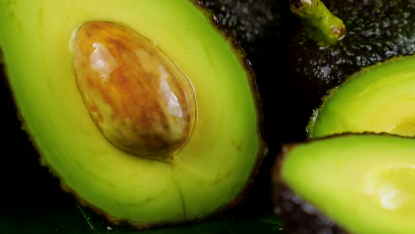 Drops of water fall on avocado fruits with leaves on a black background. Raw Fruits, healthy food.