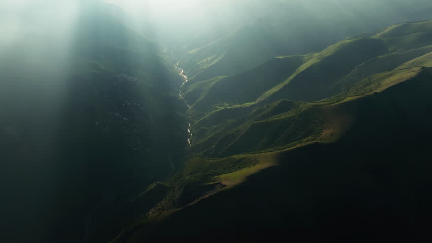 Sunbeams over Secluded Mountain Valley. Sunbeams breaking through clouds onto a secluded mountain valley, as viewed from above.
