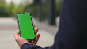 Hands holding green smartphone on street closeup. Businessman in suit videocall reading email messages in chroma key device. Unrecognized employee manager taking break watching online news outside.