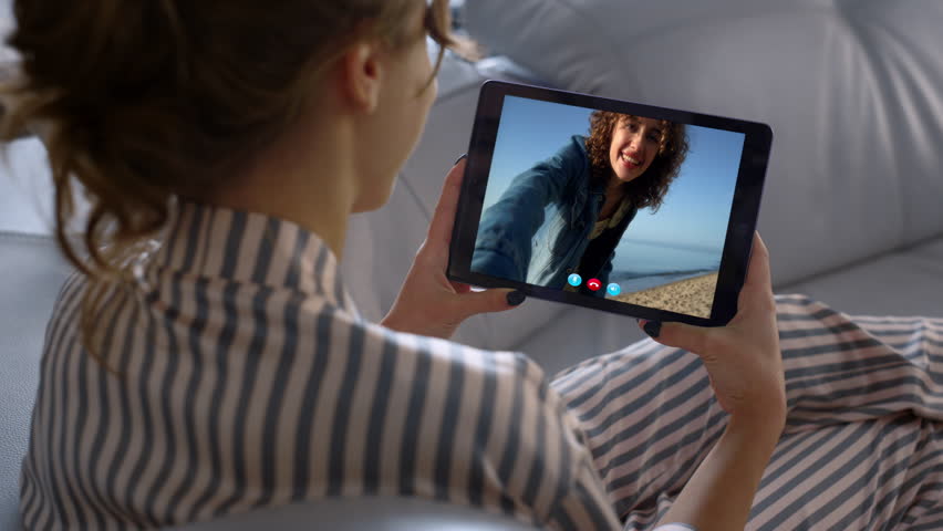 Girl talking tablet online indoors closeup. Joyful friends video calling online on travel vacation. Unknown woman chatting with computer web camera shoulder view. Happy smiling partner waving hand. Royalty-Free Stock Footage #3442163409