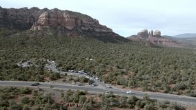 Red rock mountains and buttes in Sedona, Arizona with cars driving on the road with drone video wide shot stable.