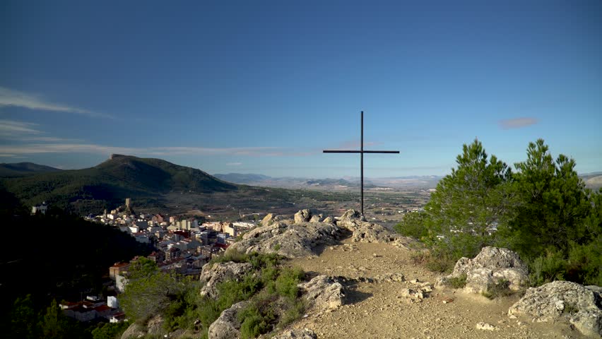 Metallic cross in the peak of a mountain, landscape with a town on background.