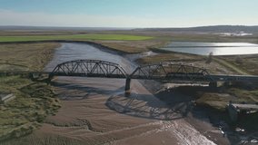 An aerial drone clip of a passenger train crossing a bridge over water in a peaceful countryside setting.