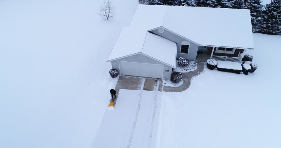 An aerial view of a homeowner shoveling snow from the driveway at a home in a typical Pennsylvania neighborhood. Pittsburgh suburbs.  	