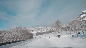 POV video of a daytime drive through the snowy roads of Norway's Western Fjords, surrounded by tall, snow-covered mountains with trees. Norwegian mountainous landscape in winter.