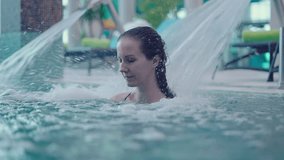 Wellness spa - young white woman in her 30s relaxing enjoying back and neck massage with water jet in pool. Leisure and lifestyle. Slow motion video.