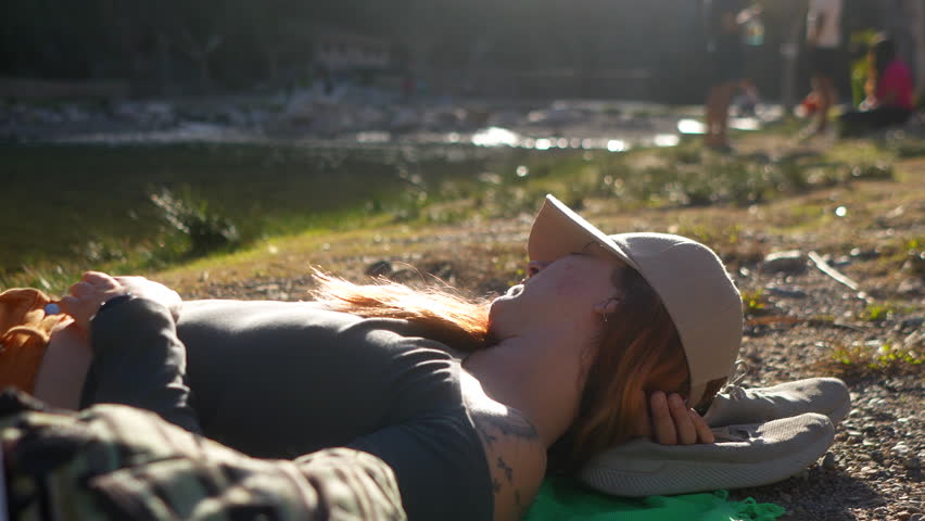 Relaxed woman laying down on a towel by the riverbank, soaking up the sun.