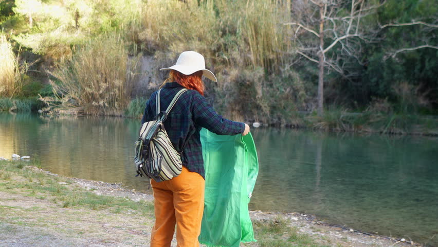 Woman by the river folding a green blanket with a smile.