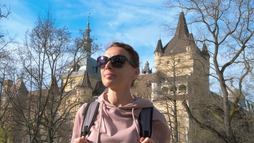 Free time by budapest castle. A cute tourist lady pass her holiday time in the city park with historical castle against blue sky.