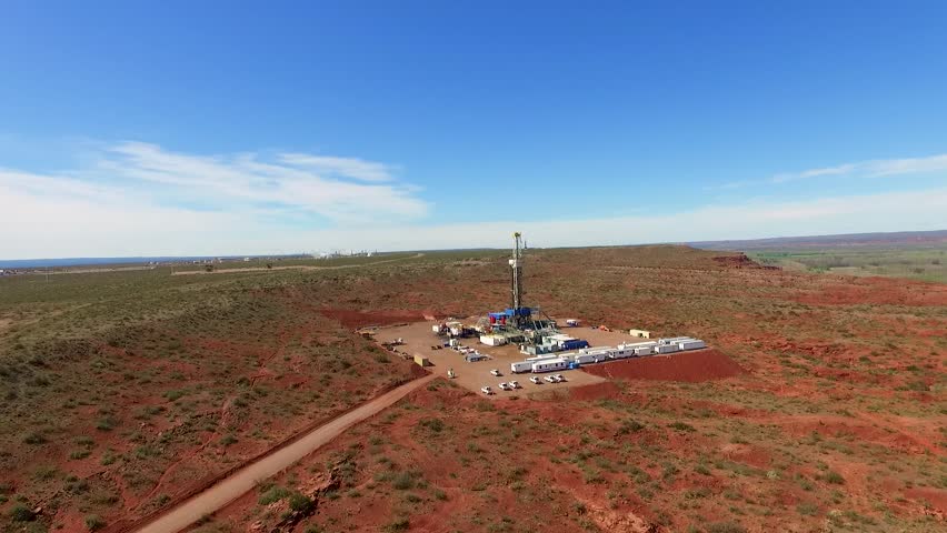 A fracking site in a vast, arid landscape under a clear blue sky, with machinery and vehicles, aerial view