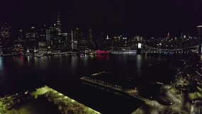 Drone aerial view of downtown NYC New York City lower Manhattan city buildings and skyscrapers on a dark night past dusk, with many lights, traffic, and glow