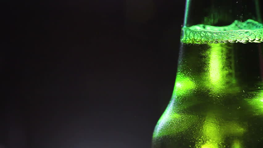 Drop of condensate drains on a green bottle of beer.