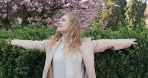 Video portrait of a beautiful young blonde woman in a beige coat in a spring park.