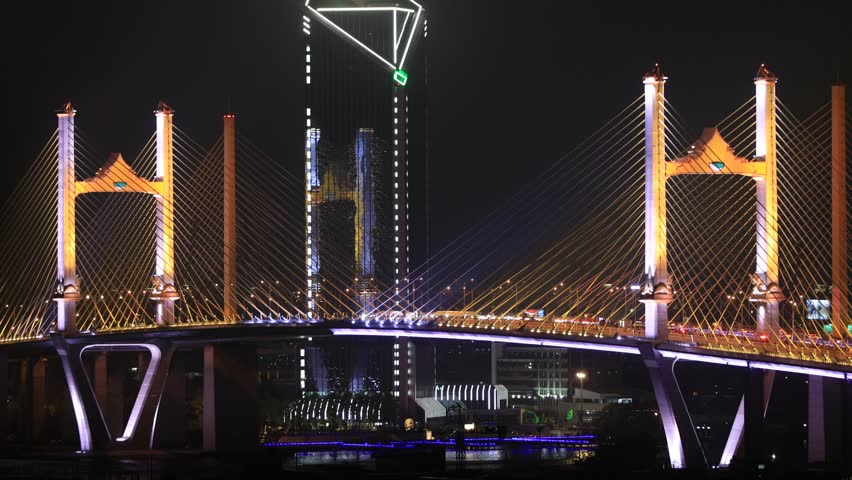 Blurred video background of colorful night lights. Beautiful bokeh is created along the bridge over the river and there is heavy traffic.