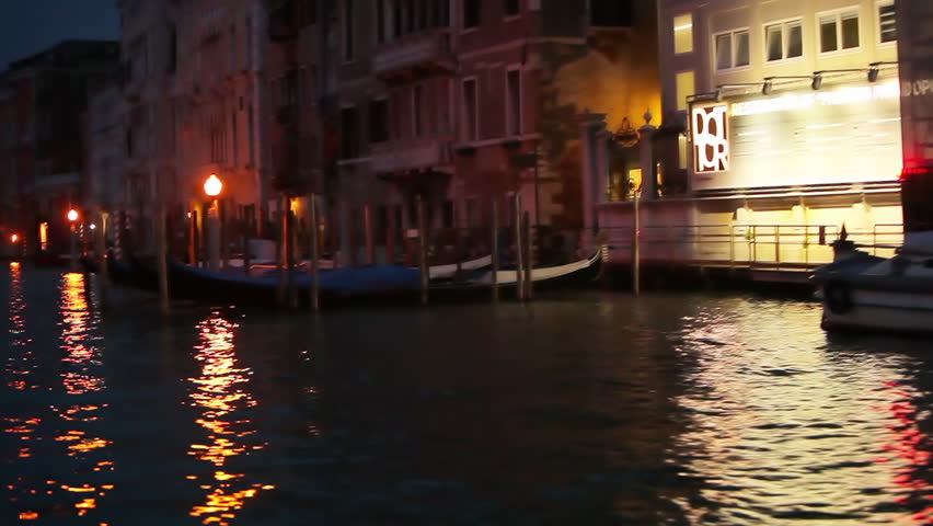Gondola floating past dark buildings and a passenger boat