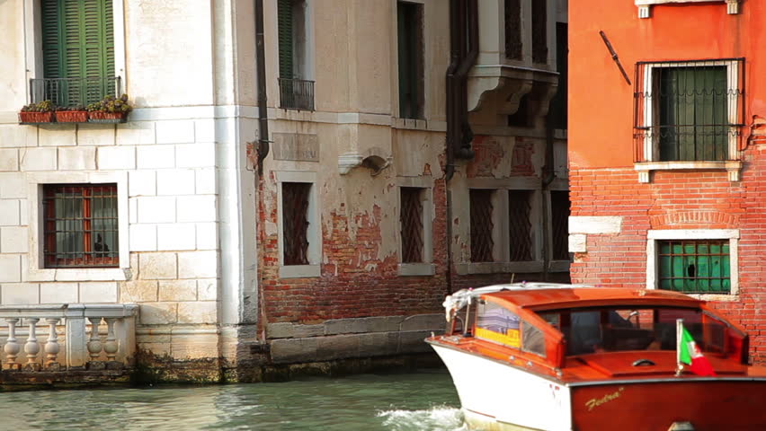 Orange motorboat driving through canal in Venice.