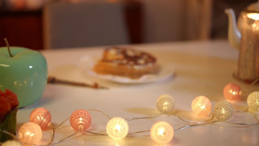 In the foreground is a switched-on garland on a festive table. Out of focus, a half-eaten birthday cake with a knife