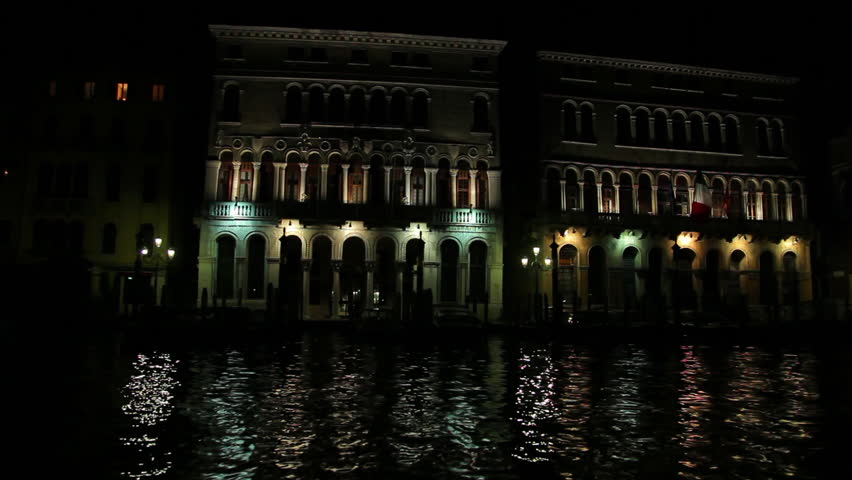 A gondola and large boat pass through the shot of the Grand Canal at night. The
