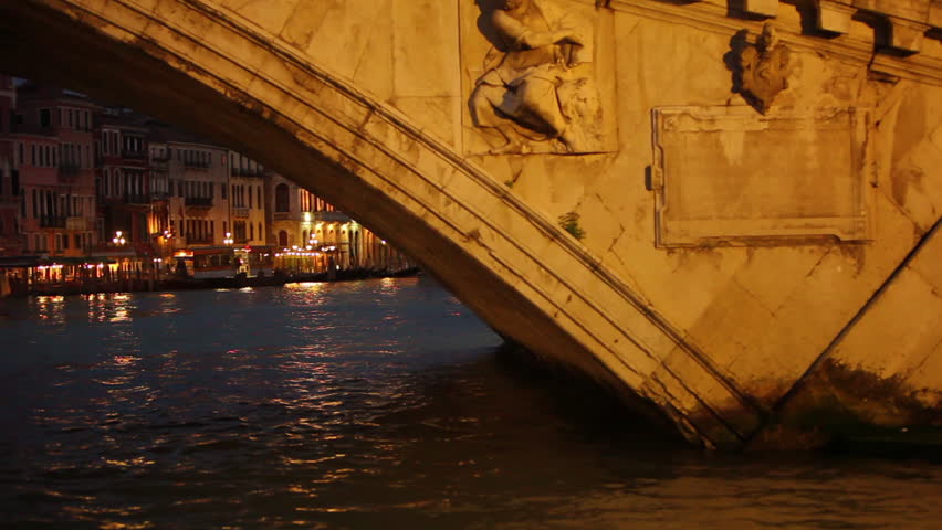 Floating under a bridge revealing low lit buildings in Venice Italy