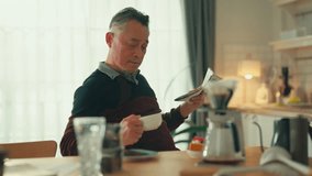 Asian male man gray hair senior retired enjoying coffee breakfast at kitchen counter weekend while reading newspaper Smiling senior man with book while sitting in kitchen at home healthy lifestyle - Powered by Shutterstock - Get 15% off with code: PIKWIZARD15