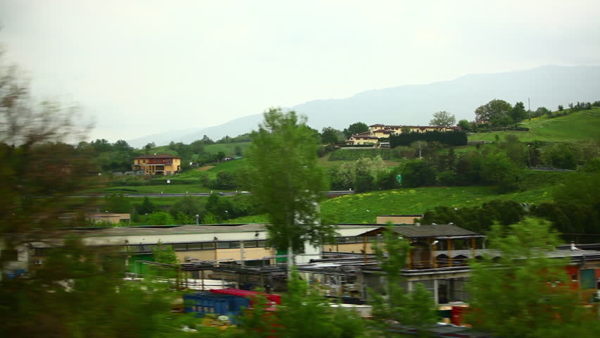 A tracking shot of warehouses and countryside in Italy captured during a train