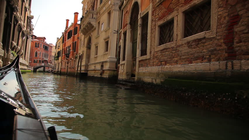 A tracking shot of a narrow canal. The front of the gondola is seen as the