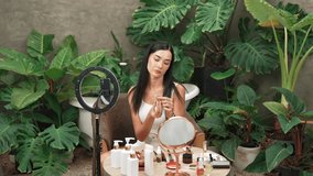 Beautiful content creator making natural beauty and cosmetic tutorial at green plant leave garden video. Beauty blogger showing how to apply beauty care to social medial audience. Blithe