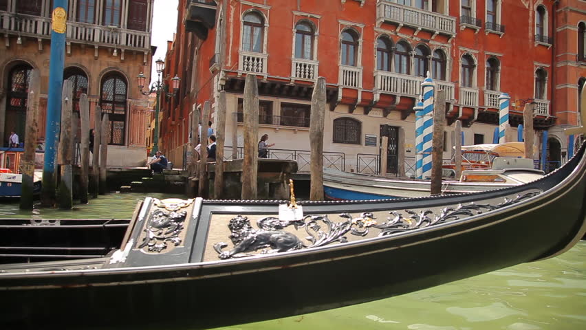 A gondola navigates around the docks on a canal. Old, colorful buildings pass by