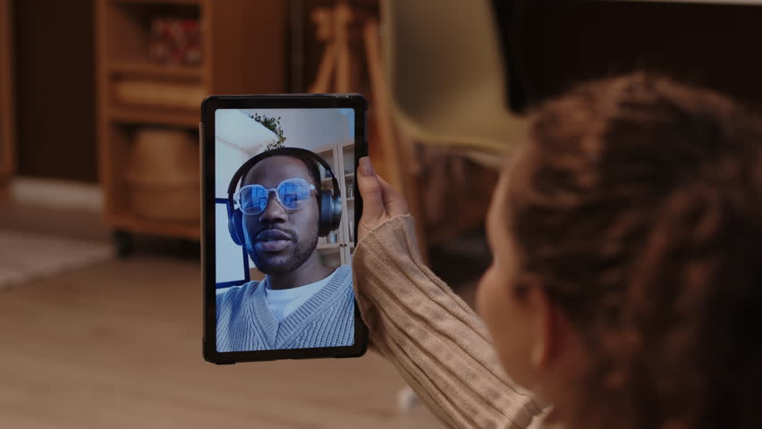 Over shoulder of Caucasian girl video calling her African American boyfriend through digital tablet while at home, having long distance relationship Royalty-Free Stock Footage #3442679287