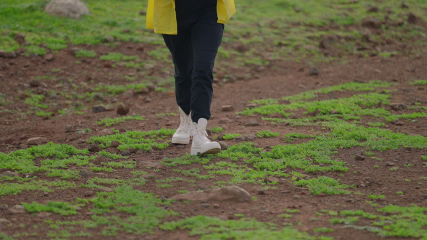 Close-up white hiking boots for travel. Camera follows woman on trip or adventure. Young traveller or travel blogger walk in beautiful mountain valley. Woman hiker in yellow raincoat with backpack