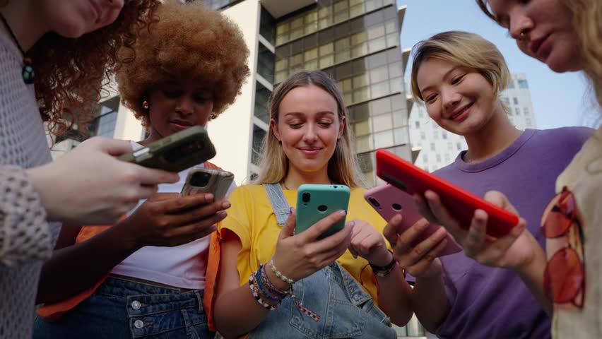 Diverse group only women looking at happy cell phone. Low angle view of girl friends addicted to technology. People gathered in circle using mobile. New generations and communication social networks