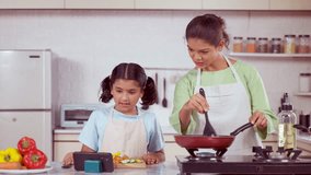 Happy mother and daughter try cooking new recipe by watching video from mobile phone at kitchen - concept of technology, weekend activities and relationship bonding