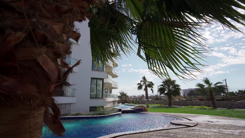Beachfront luxury apartments with blue infinity pool, palm trees in vibrant tropical setting. Real estate investment in exclusive properties with ocean view. Royalty-Free Stock Footage #3442755265