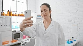 A young woman in a lab coat using a smartphone in a bright laboratory setting.