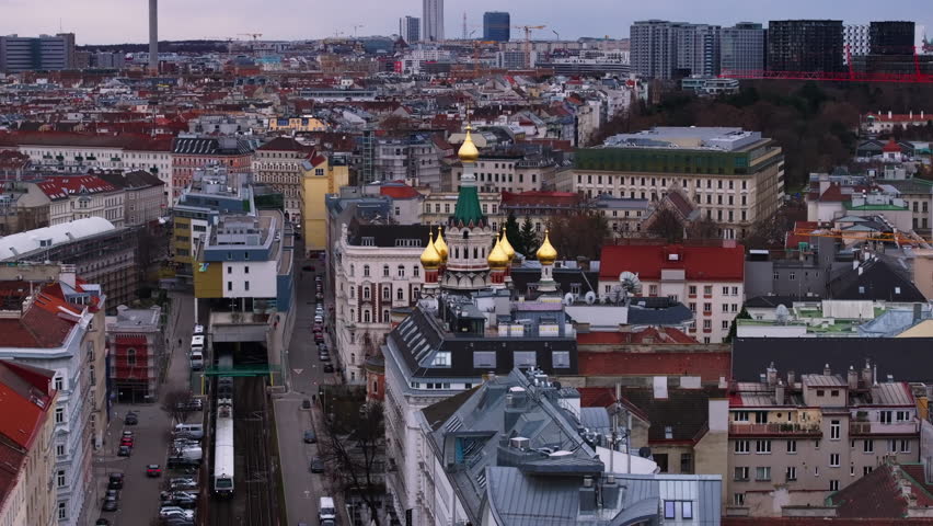 Aerial slide and pan footage of orthodox church surrounded by buildings and railway line in city. Vienna, Austria, December 2, 2023