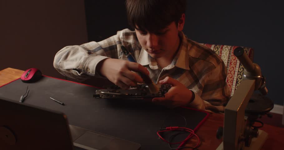 Enthusiastic teenager cleans a computer video card with a brush from dust. Repair and restoration of equipment. Hobby. Live camera effect