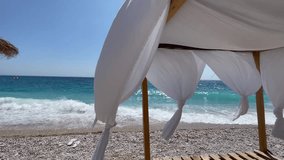 White beach canopies. Gazebo on the beach by the sea. Rocky beach. Curtains develop in the wind. Day light summer. South of Albania, Livadi Beach in Himare. horizontal video, HD 
