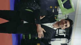 Vertical Video. Portrait of Successful Owner of Tractor Company with His Arms Crossed. Mature Farmer in Formal Suit Posing in Auto Center with Tractor in Background and Looks at Camera - Powered by Shutterstock - Get 15% off with code: PIKWIZARD15