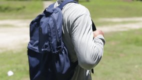 A man holds a blue backpack. A man prepares for active walking with a loose backpack.